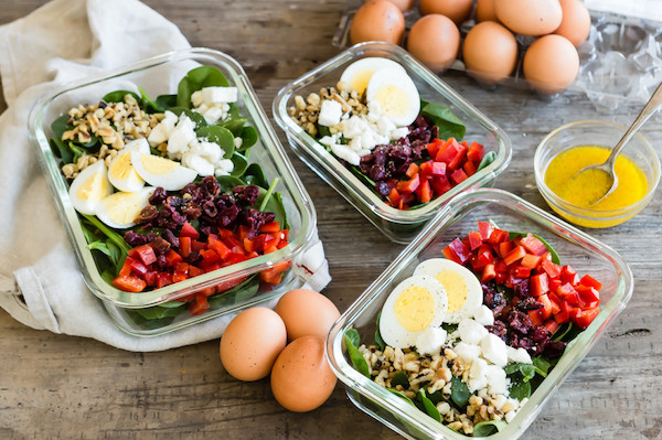 A healthy and nutritious salad featuring organic hard-boiled eggs, fresh spinach, walnuts, feta cheese, red bell pepper, and cranberries. Portioned out in meal prep containers and served with an orange zest vinaigrette. | peteandgerrys.com 