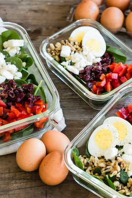 A healthy and nutritious salad featuring organic hard-boiled eggs, fresh spinach, walnuts, feta cheese, red bell pepper, and cranberries. Portioned out in meal prep containers and served with an orange zest vinaigrette. | peteandgerrys.com 