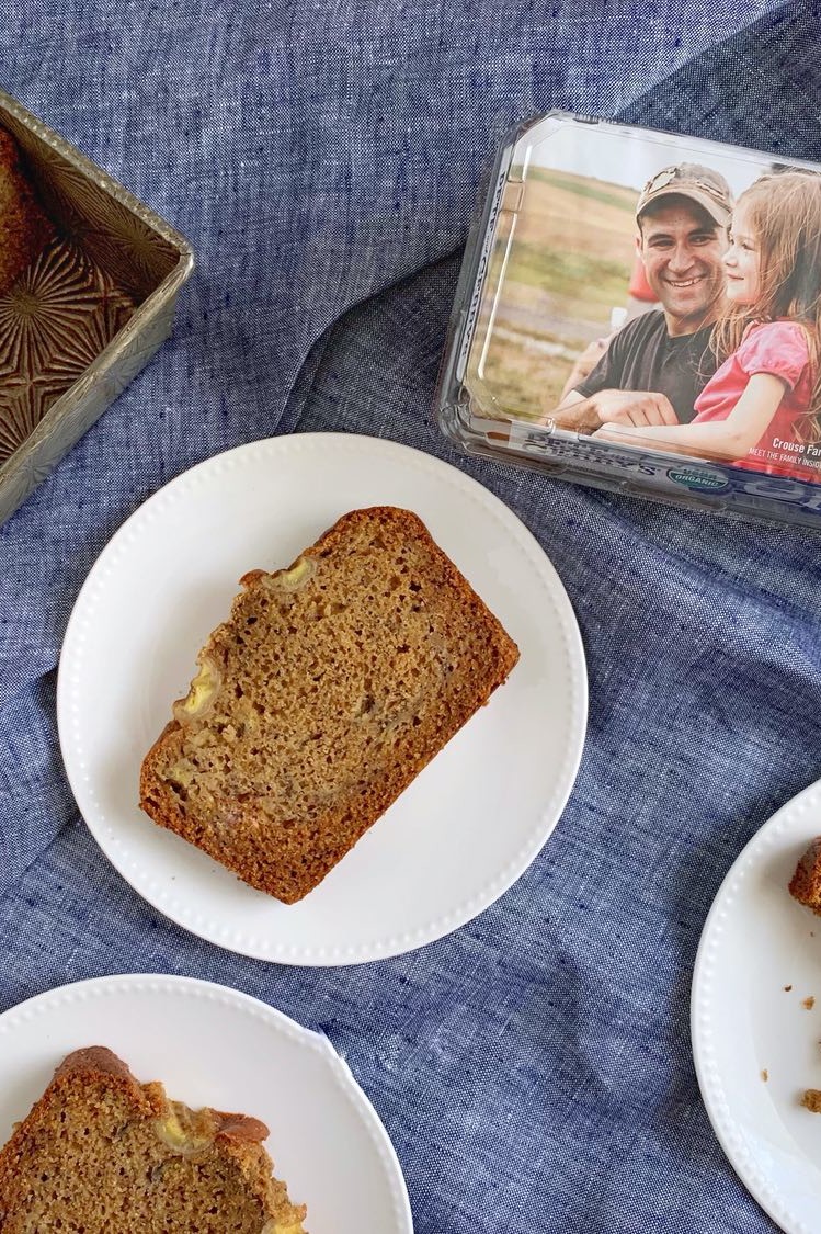 Brown butter banana bread with banana baked in top for decoration. Slices are plated on white dishes and show a moist crumb. Pete and Gerry's Organic Egg carton in the corner of the frame. | peteandgerrys.com 