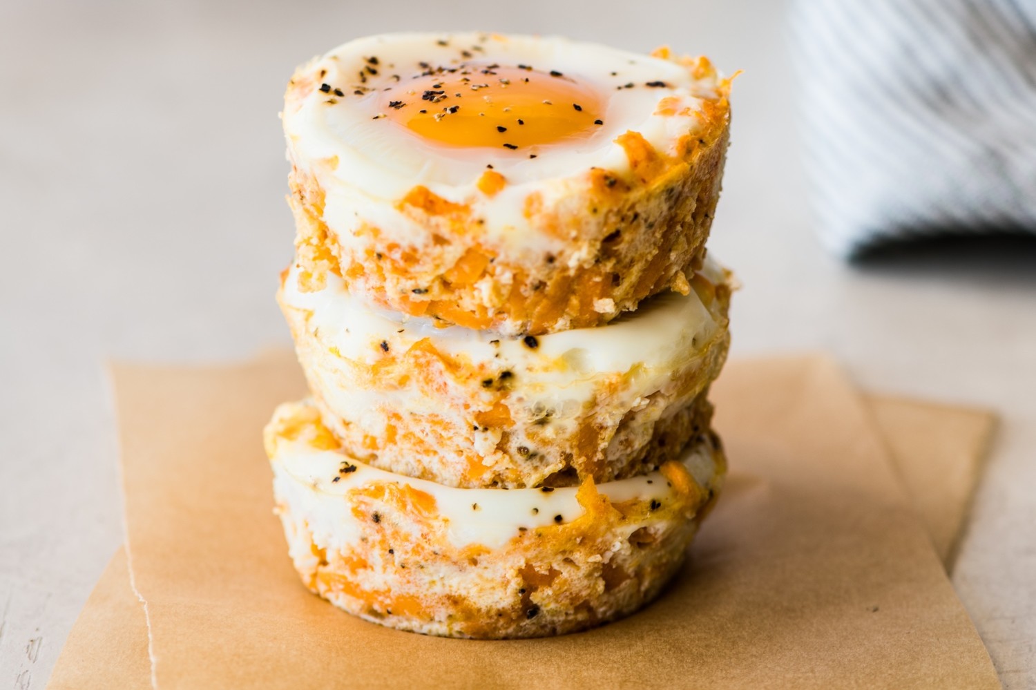 Chipotle sweet potato egg cups baked in a muffin tin. Stack of three egg cups shows layers of shredded sweet potato, cheese, chipotle powder, and eggs. | peteandgerrys.com 