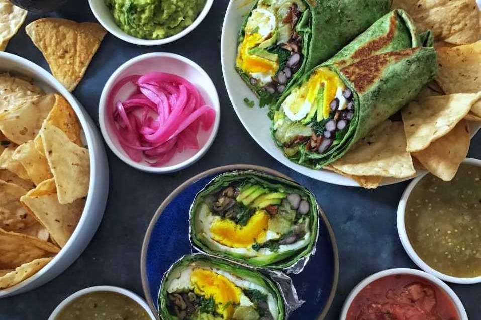 This green goddess breakfast burrito features spinach tortillas filled with collard greens, jack cheese, avocado, sweet potato, spinach, black beans, and organic eggs over easy. | peteandgerrys.com  