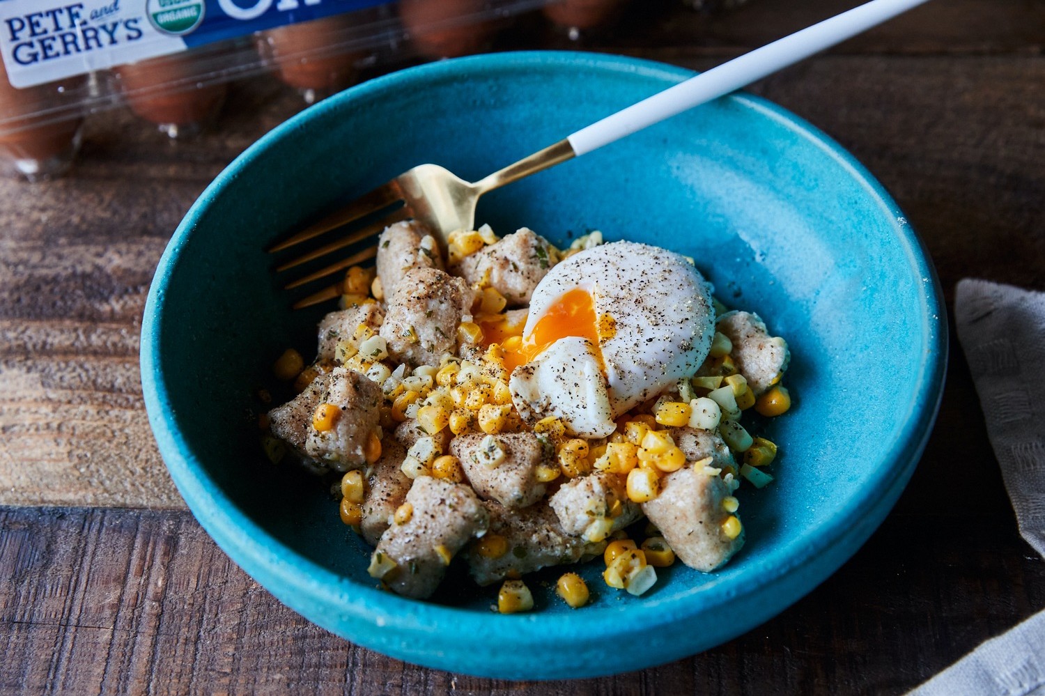 Blue bowl full of ricotta gnocchi with sweet corn, rosemary butter, and poached egg. Poached egg is missing a cut to show vibrant, deep orange yolk. | peteandgerrys.com 