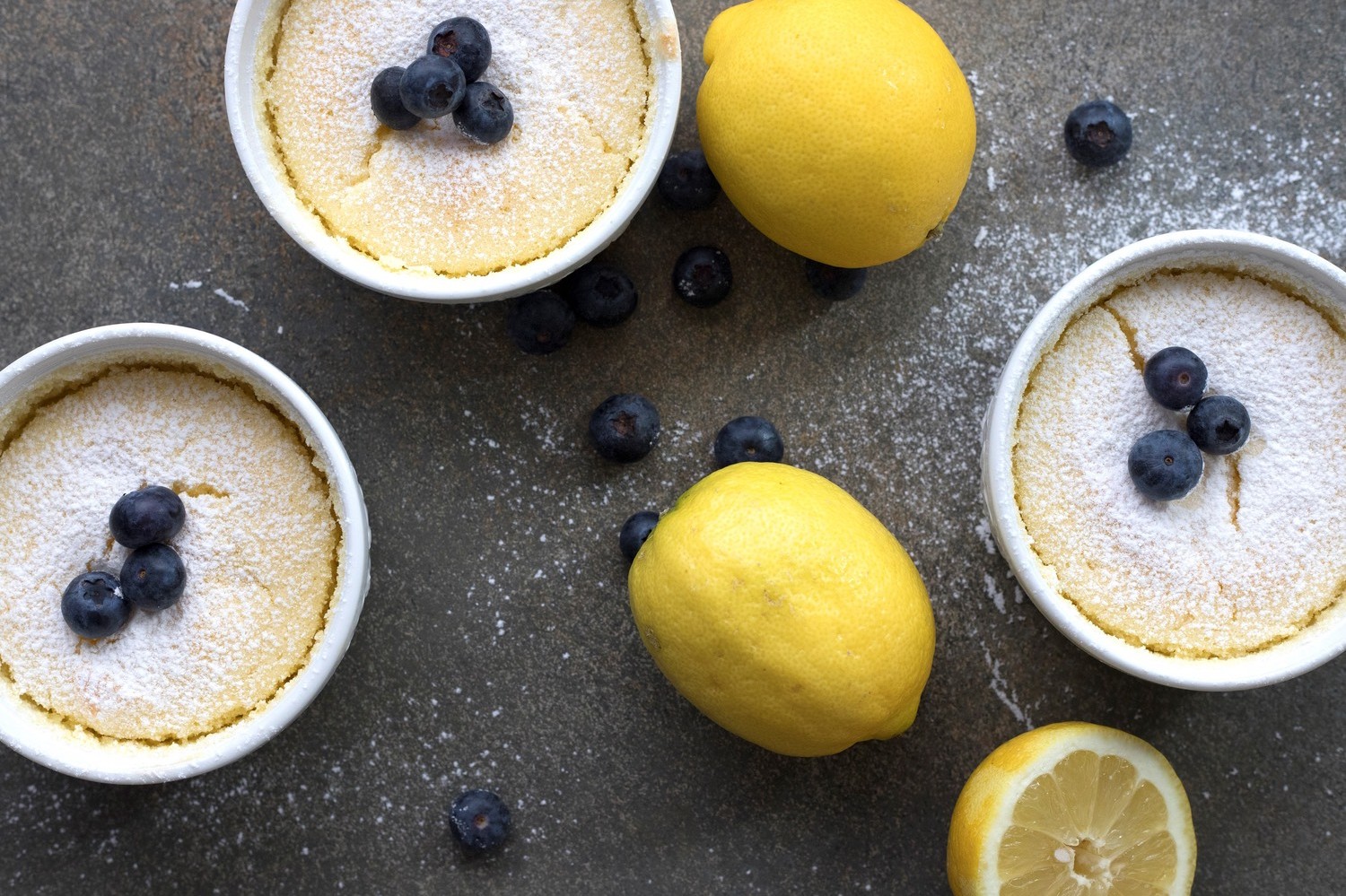 These keto-friendly lemon pudding cakes are pictured in individual ramekins. The cake is made of organic eggs, low-carb sweetener, almond flour, and fresh lemon juice. We topped our ramekins with powdered sugar and blueberries. | peteandgerrys.com 