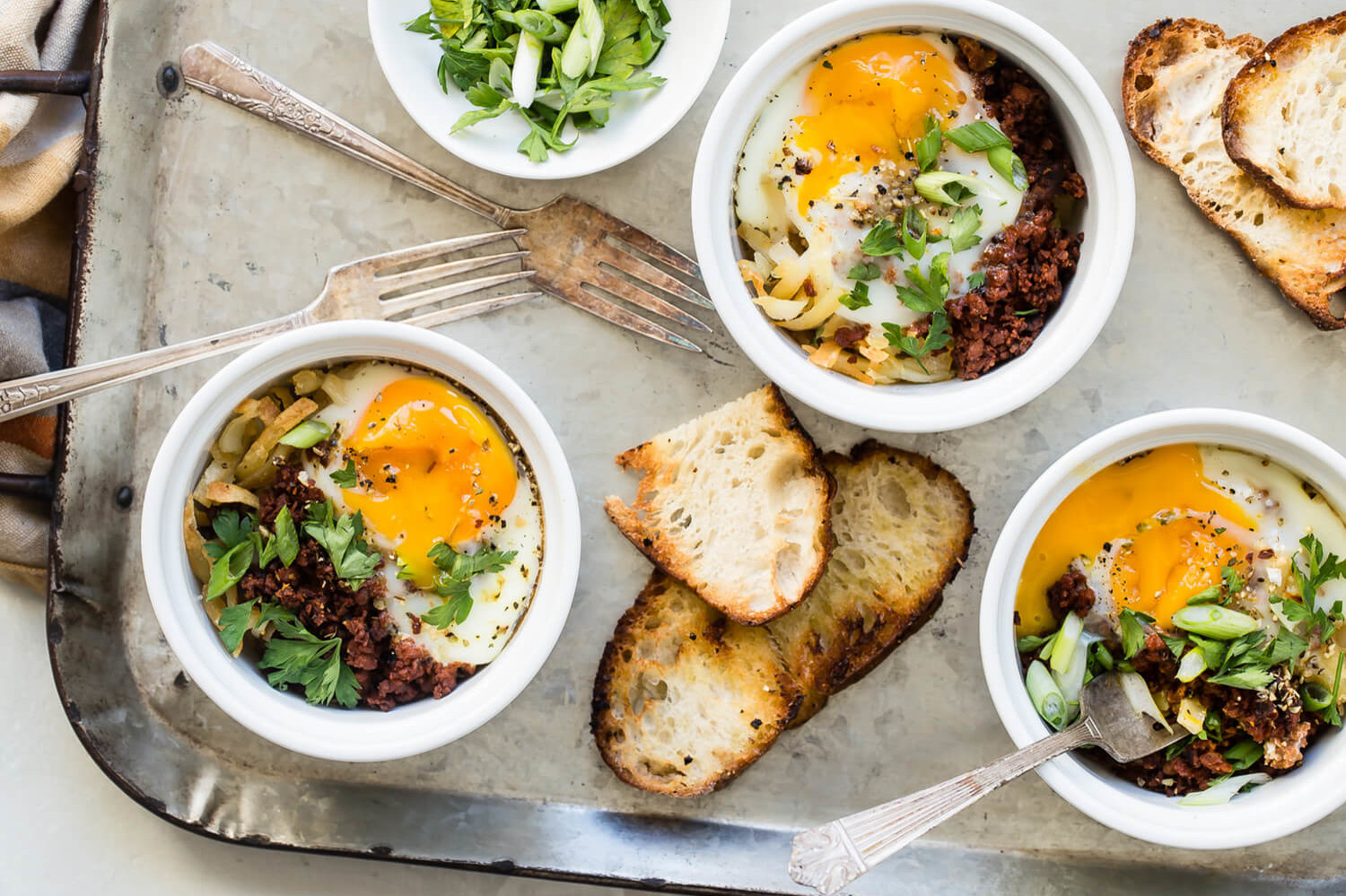 Organic eggs with runny yolks atop browned chorizo and hash browns. Each portion is baked in its own ramekin and served with toast on the side. | peteandgerrys.com