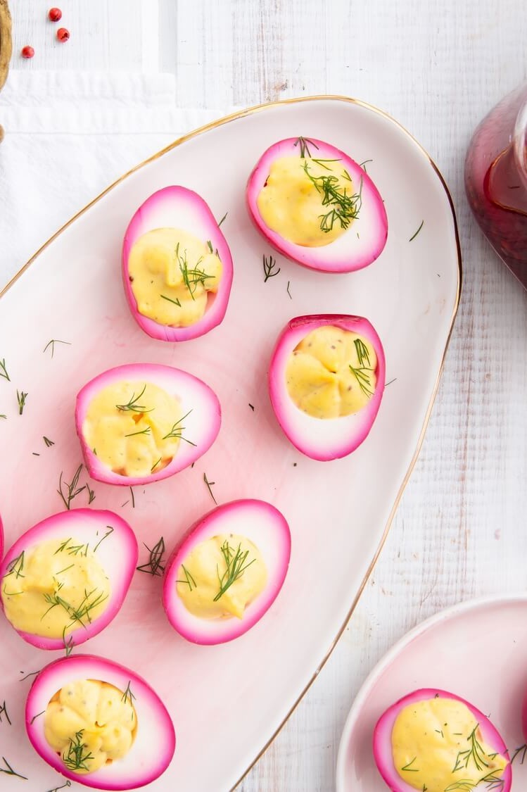 Beet pickled deviled eggs on platter. Hard-boiled eggs are soaked in beet juice overnight, resulting in a a violet exterior. Cross section shows vibrant yellow yolk filling piped into each deviled egg half. | peteandgerrys.com   