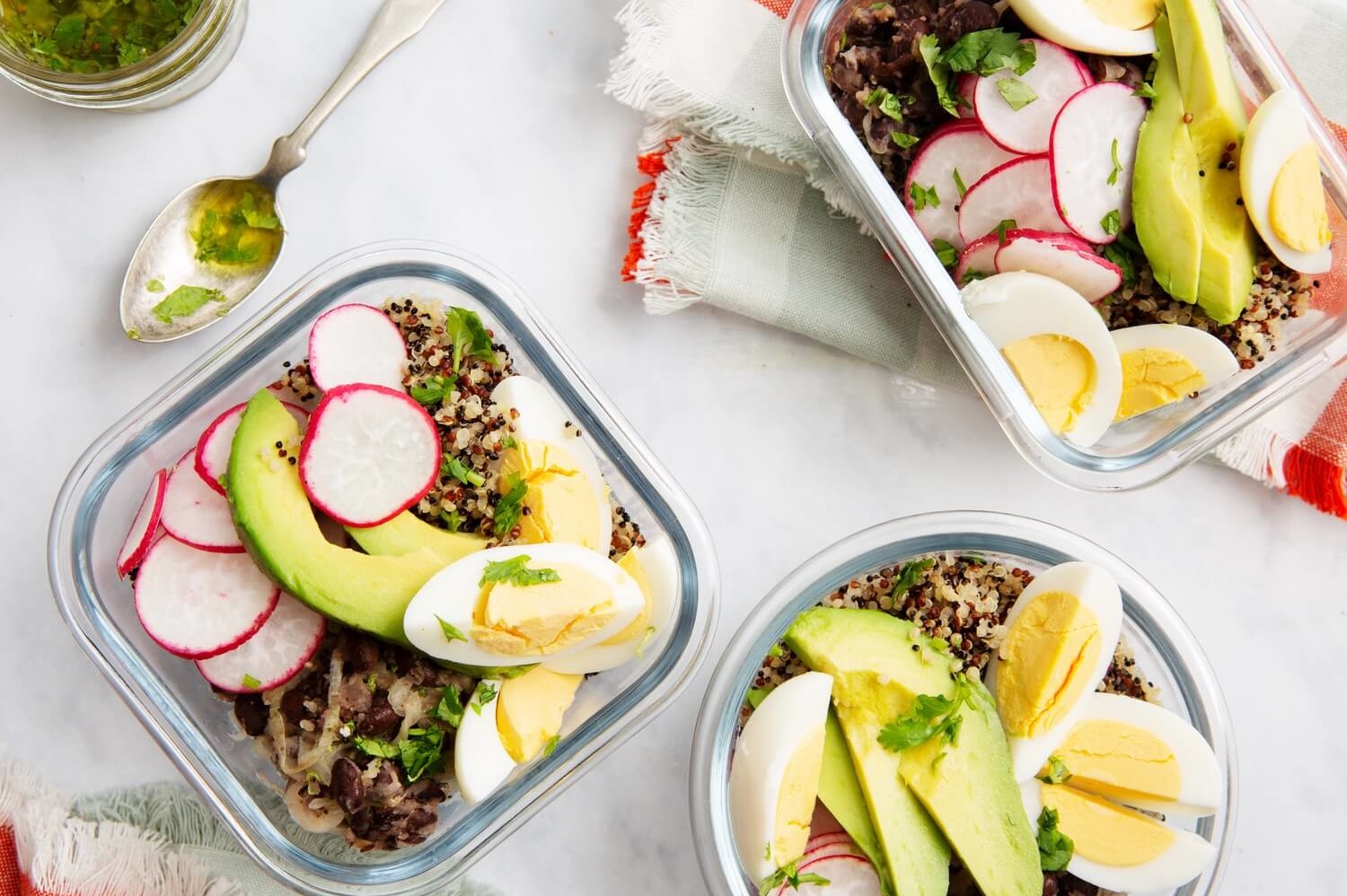 Meal prep containers filled with cooked quinoa, sliced avocado, black beans, thinly sliced radishes, and quartered organic hard-boiled eggs. Served with tangy honey lime dressing. | peteandgerrys.com