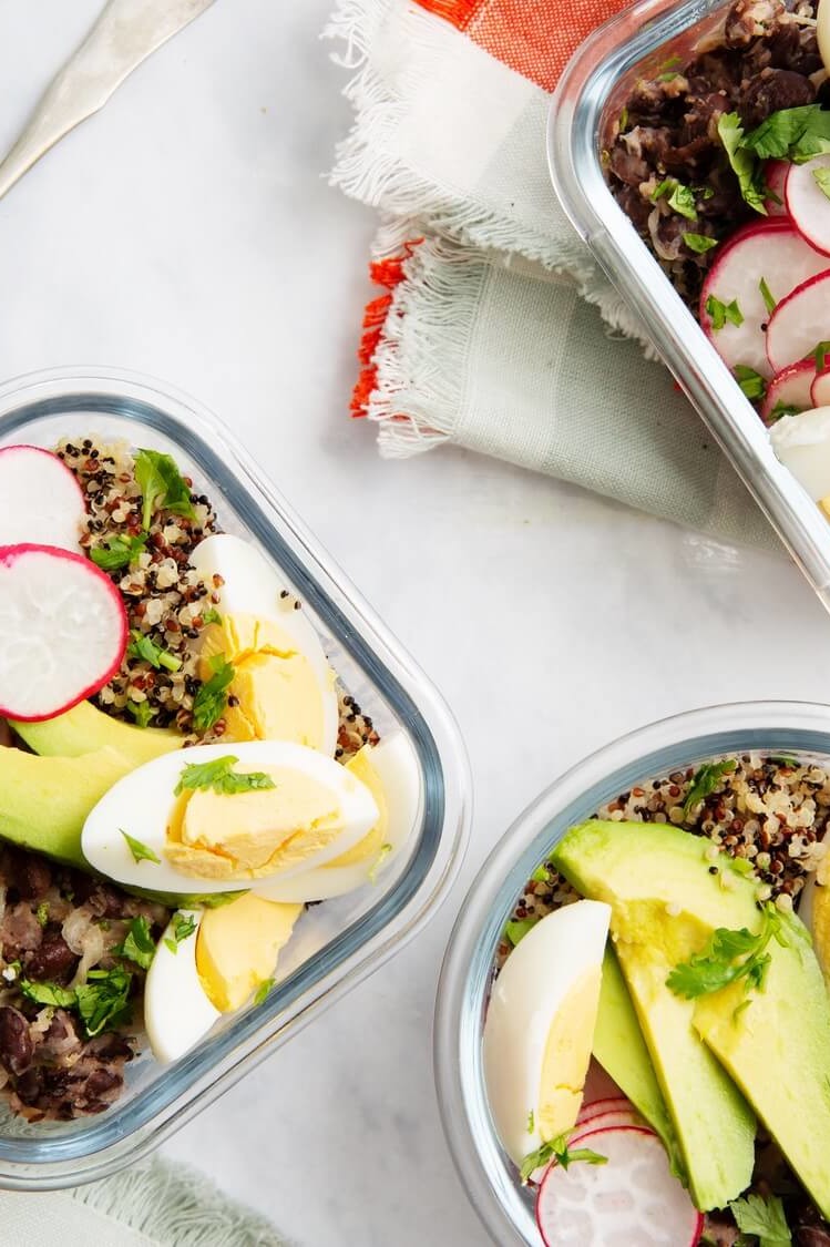 Meal prep containers filled with cooked quinoa, sliced avocado, black beans, thinly sliced radishes, and quartered organic hard-boiled eggs. Served with tangy honey lime dressing. | peteandgerrys.com