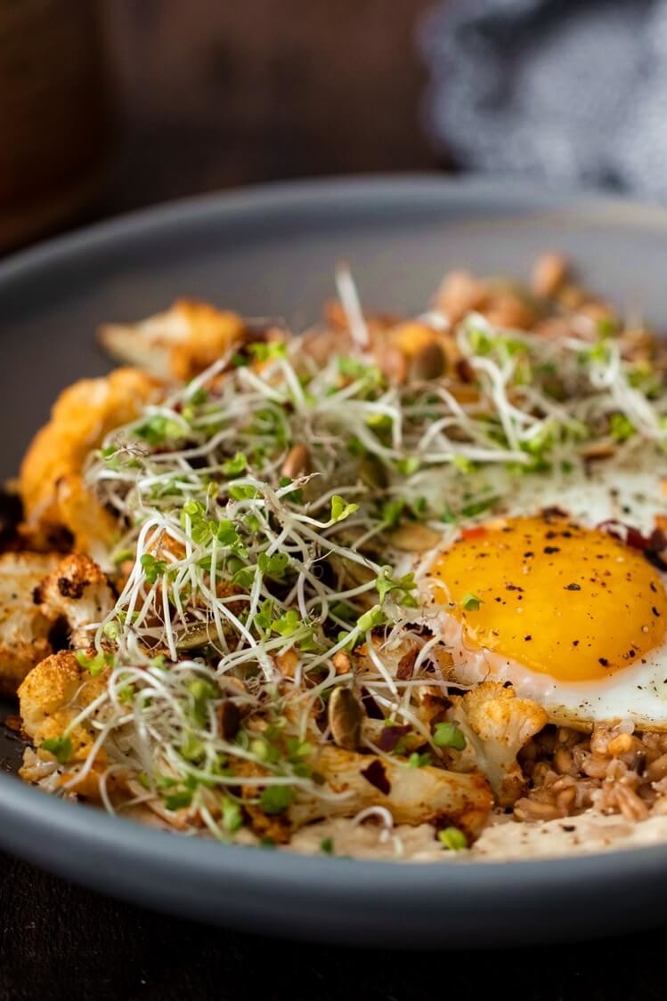 A nutritious vegetarian grain bowl for lunch or dinner. Bowl features roasted cauliflower florets, hummus, farro, microgreens, and a fried organic egg. | peteandgerrys.com 