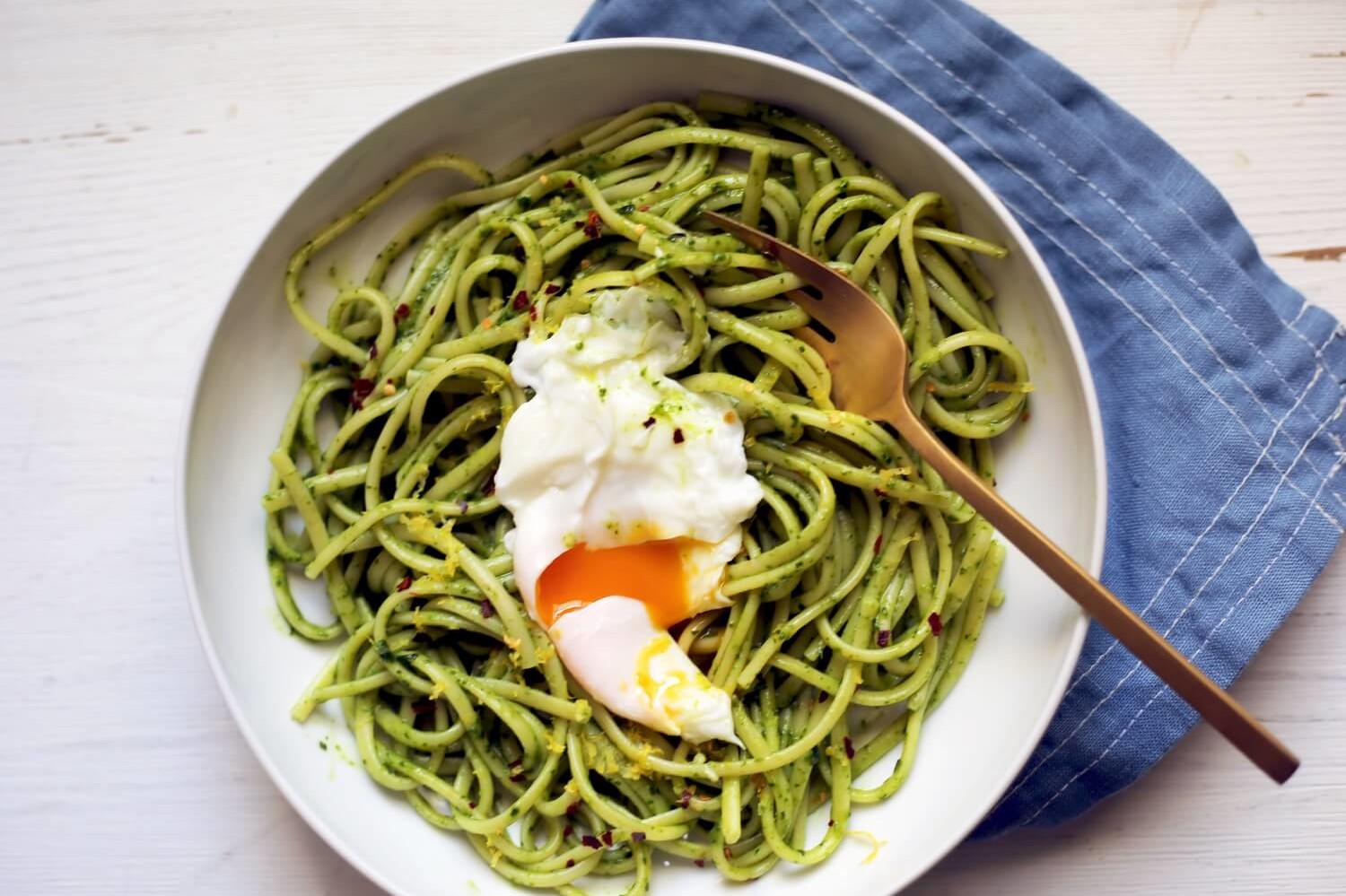 Bowl of spaghetti coated in homemade CBD-infused pesto. Topped with a poached egg, which has been cut open to allow the deeply golden yolk to flow into the pasta. | peteandgerrys.com 