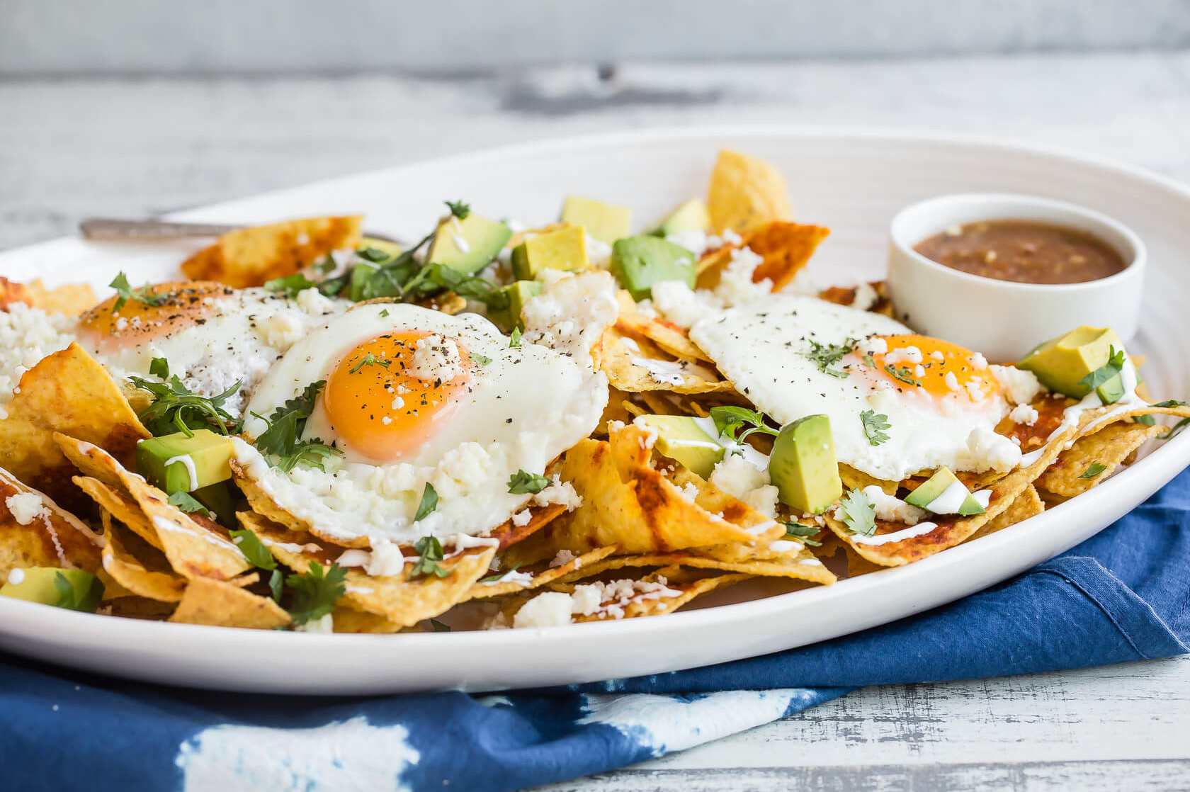 A recipe for chilaquiles, a traditional Mexican dish made with tortilla chips baked in red chili sauce. Served on a platter with fried eggs, diced avocado, fresh cilantro, and queso fresco. | peteandgerrys.com 