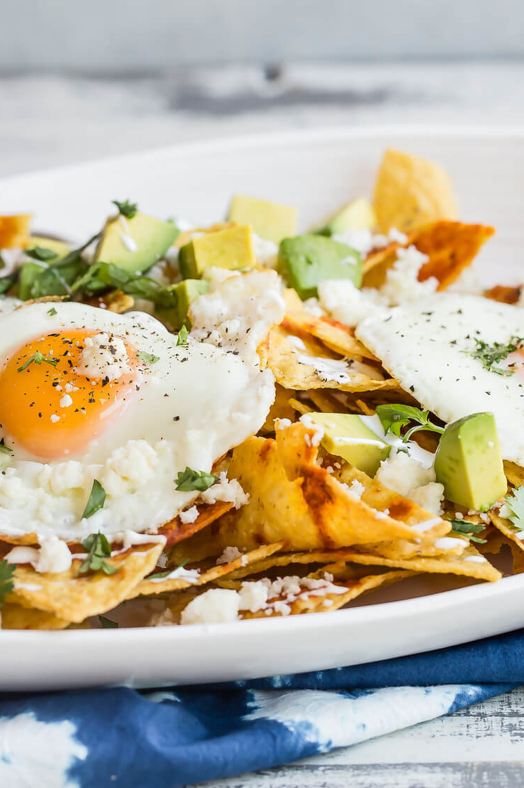 A recipe for chilaquiles, a traditional Mexican dish made with tortilla chips baked in red chili sauce. Served on a platter with fried eggs, diced avocado, fresh cilantro, and queso fresco. | peteandgerrys.com 