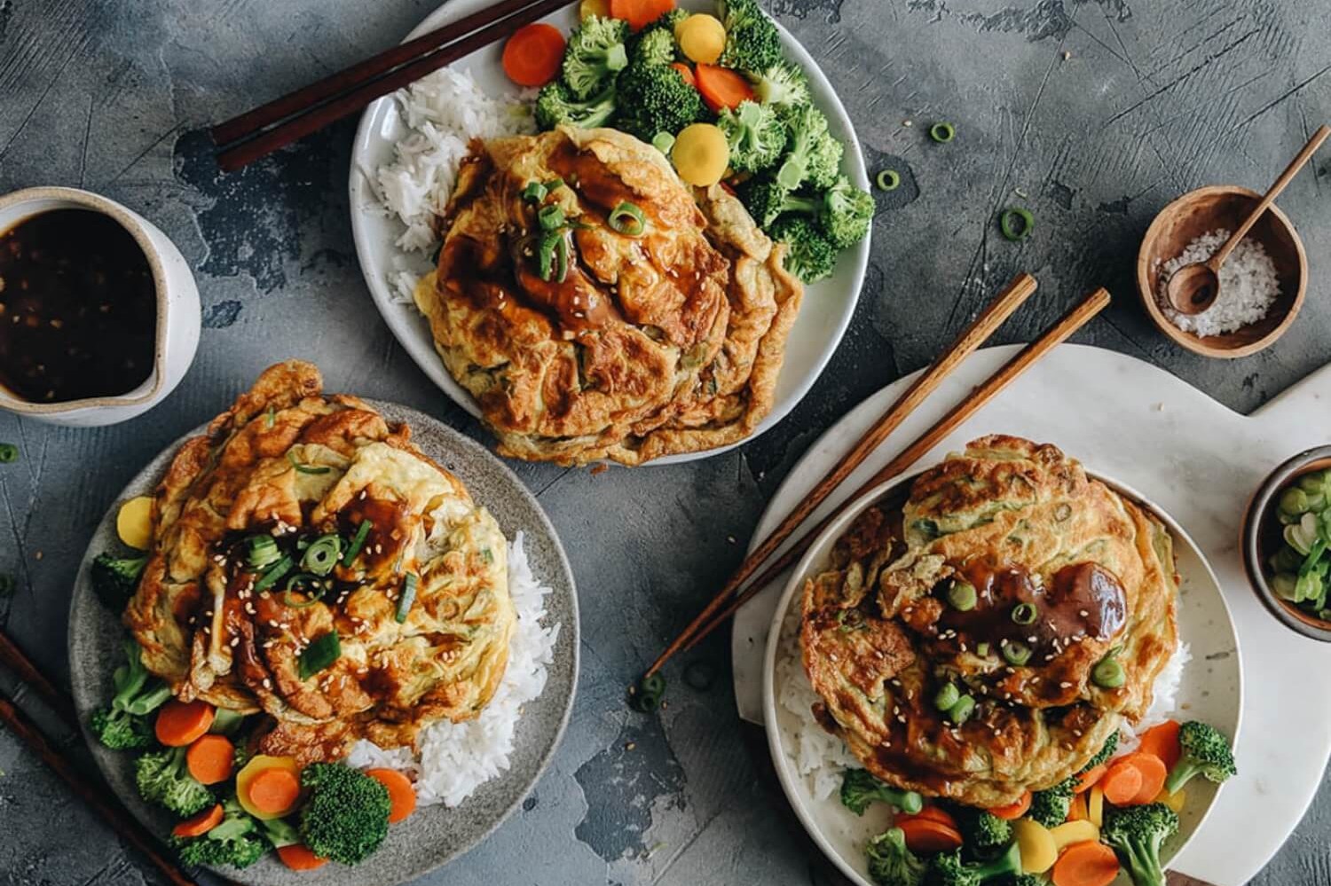 Egg foo young, a traditional Cantonese dish featuring crispy, browned pan-seared eggs mixed with bell peppers, green onions, and white pepper. Served with a rich brown gravy alongside steamed vegetables and white rice. | peteandgerrys.com 