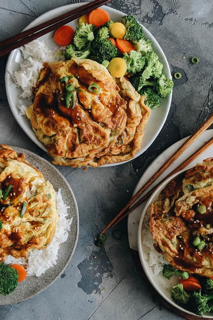 Egg foo young, a traditional Cantonese dish featuring crispy, browned pan-seared eggs mixed with bell peppers, green onions, and white pepper. Served with a rich brown gravy alongside steamed vegetables and white rice. | peteandgerrys.com 