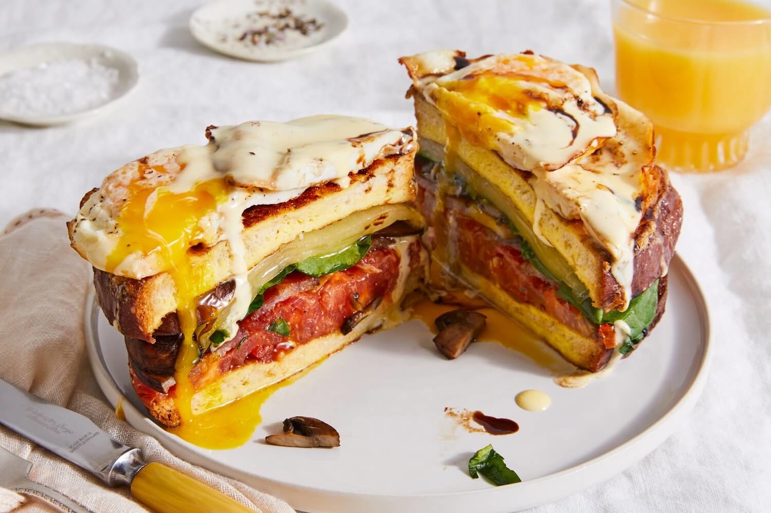 This towering sandwich features a total of eight layers, including bacon, cheese, eggs, mushrooms, spinach, and tomatoes. The sandwich is topped with a rich hollandaise sauce and balsamic reduction. | peteandgerrys.com  