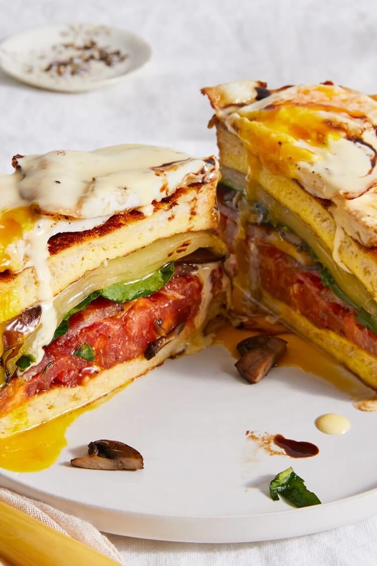 This towering sandwich features a total of eight layers, including bacon, cheese, eggs, mushrooms, spinach, and tomatoes. The sandwich is topped with a rich hollandaise sauce and balsamic reduction. | peteandgerrys.com  