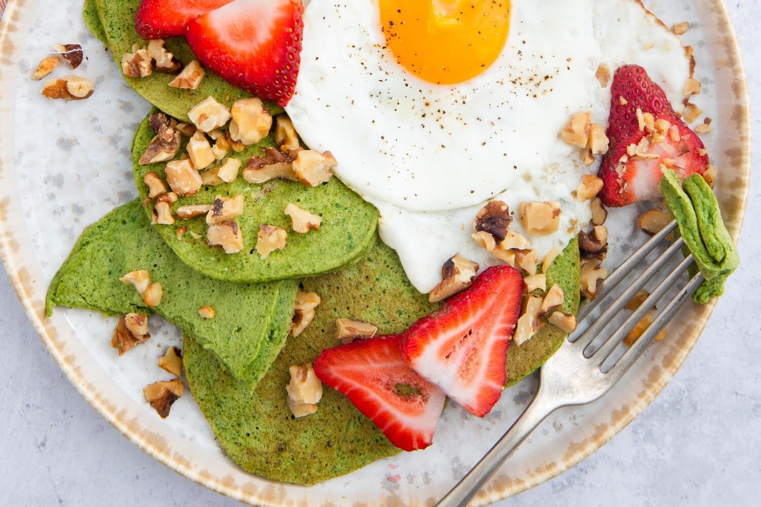 This green pancakes recipe features pancakes based with spinach and bananas. Our pancakes are topped with sliced strawberries, walnuts, and a fried egg. | peteandgerrys.com 