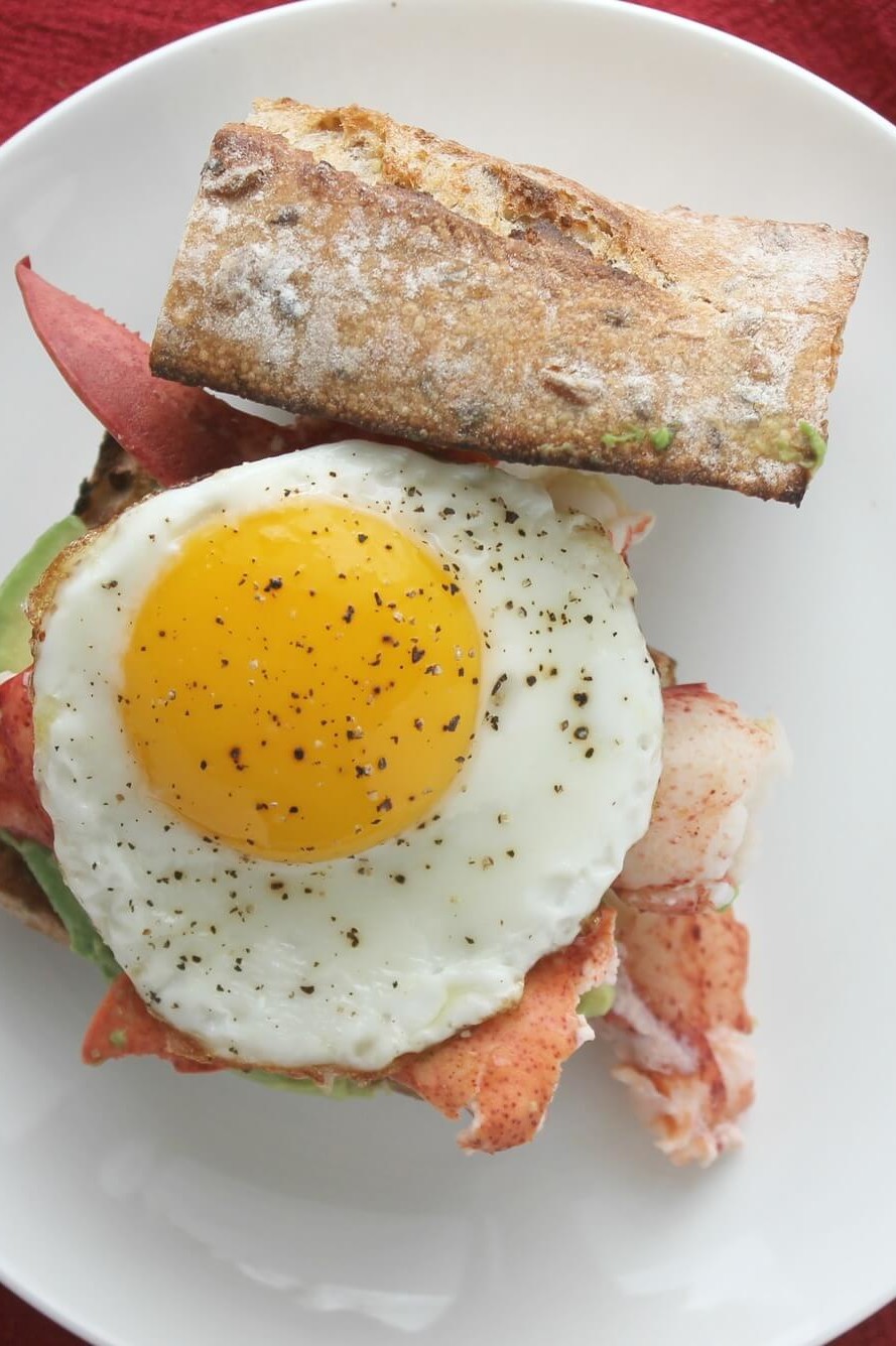 This lobster, egg, and avocado breakfast sandwich is the perfect way to start or finish the summer season. Pictured is a crusty baguette topped with Maine lobster, avocado slices, and an organic egg. | peteandgerrys.com 