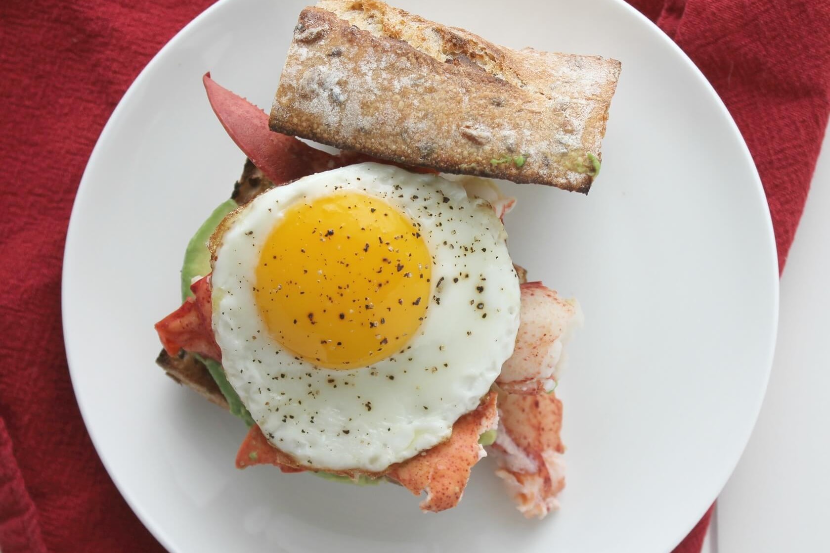 This lobster, egg, and avocado breakfast sandwich is the perfect way to start or finish the summer season. Pictured is a crusty baguette topped with Maine lobster, avocado slices, and an organic egg. | peteandgerrys.com 