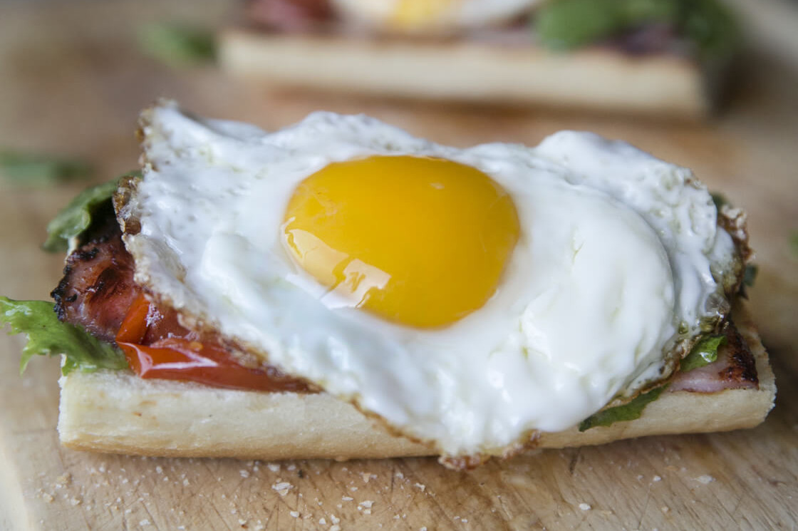 This open-faced egg sandwich features a fried egg on top of thick-sliced tomatoes, greens, and crusty french bread. | peteandgerrys.com 