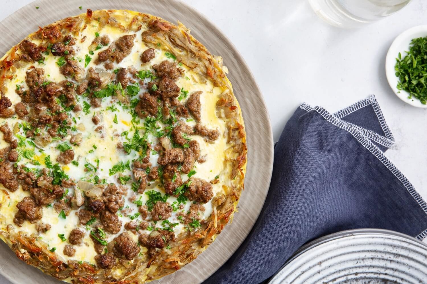 This potato quiche is cooked with an organic egg filling until golden brown. Pictured on top of the quiche are crumbled ground beef, shredded cheese, and parsley. | peteandgerrys.com 