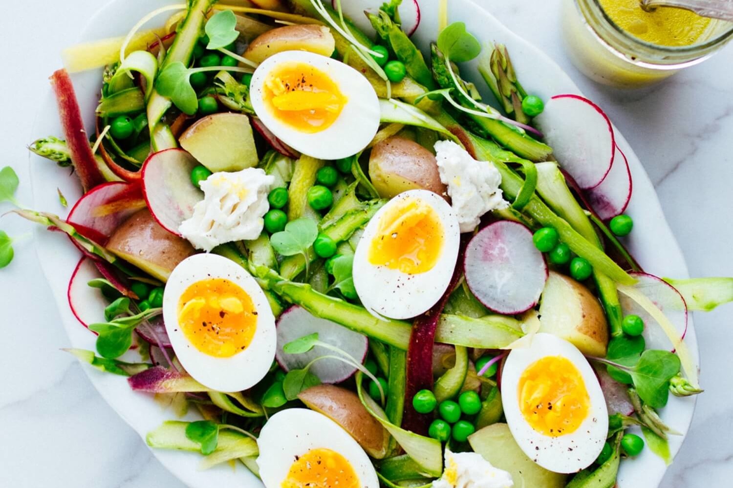 This shaved asparagus salad is light and refreshing. Pictured is bright green asparagus, sweet peas, radishes, goat cheese, and soft boiled eggs. | peteandgerrys.com 