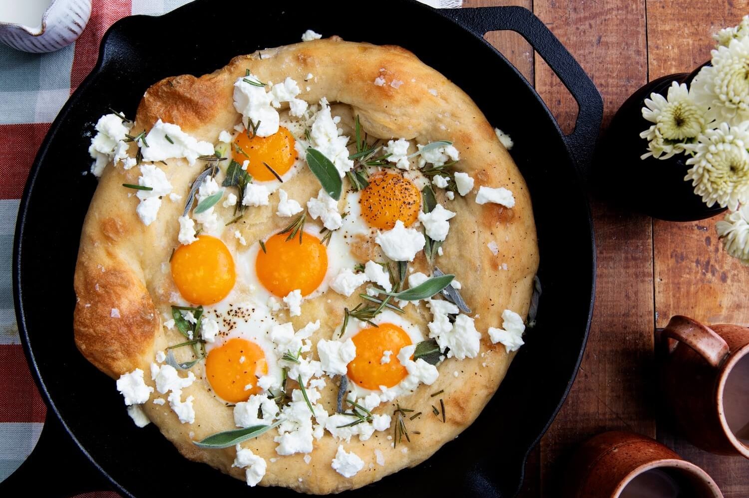 This sunny side up egg pizza features fluffy dough, topped with feta cheese, organic egg yolks, fresh sage, and rosemary. | peteandgerrys.com 