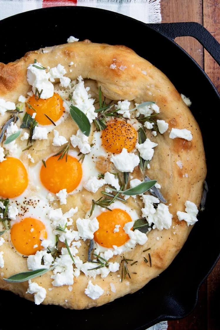 This sunny side up egg pizza features fluffy dough, topped with feta cheese, organic egg yolks, fresh sage, and rosemary. | peteandgerrys.com 