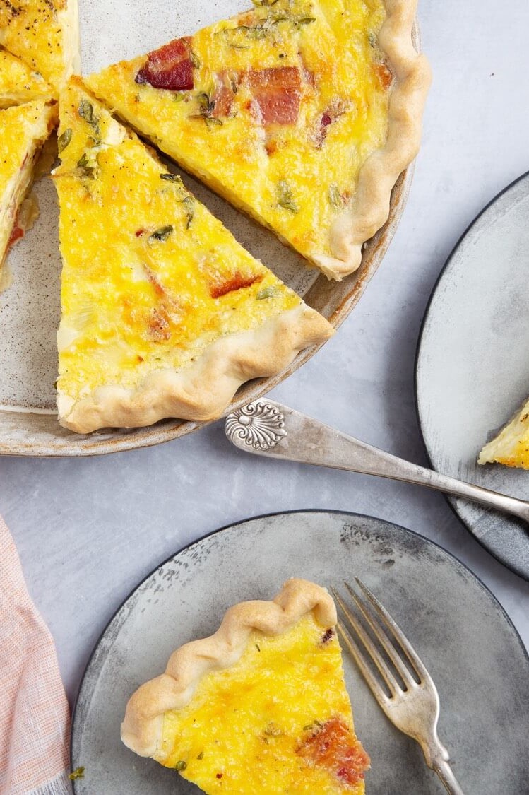 Pictured is a bright yellow swiss onion quiche with pieces of bacon and fresh thyme. This recipe features homemade crust and organic eggs. | peteandgerrys.com 