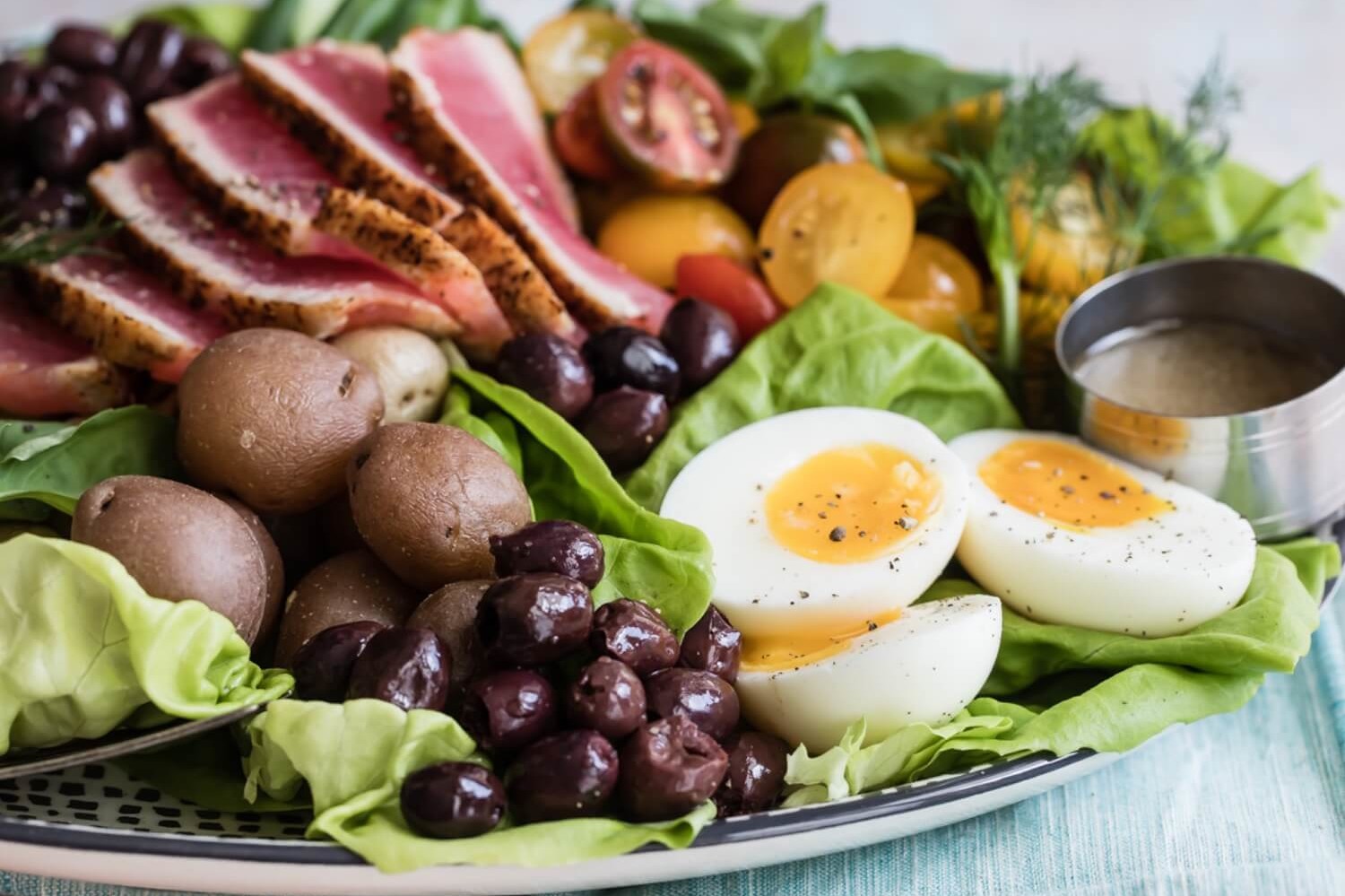 This colorful Niçoise salad features mixed greens, sliced ahi tuna, jammy soft-boiled eggs, olives, and a variety of other mix-ins. Served with a light white wine vinaigrette. | peteandgerrys.com  