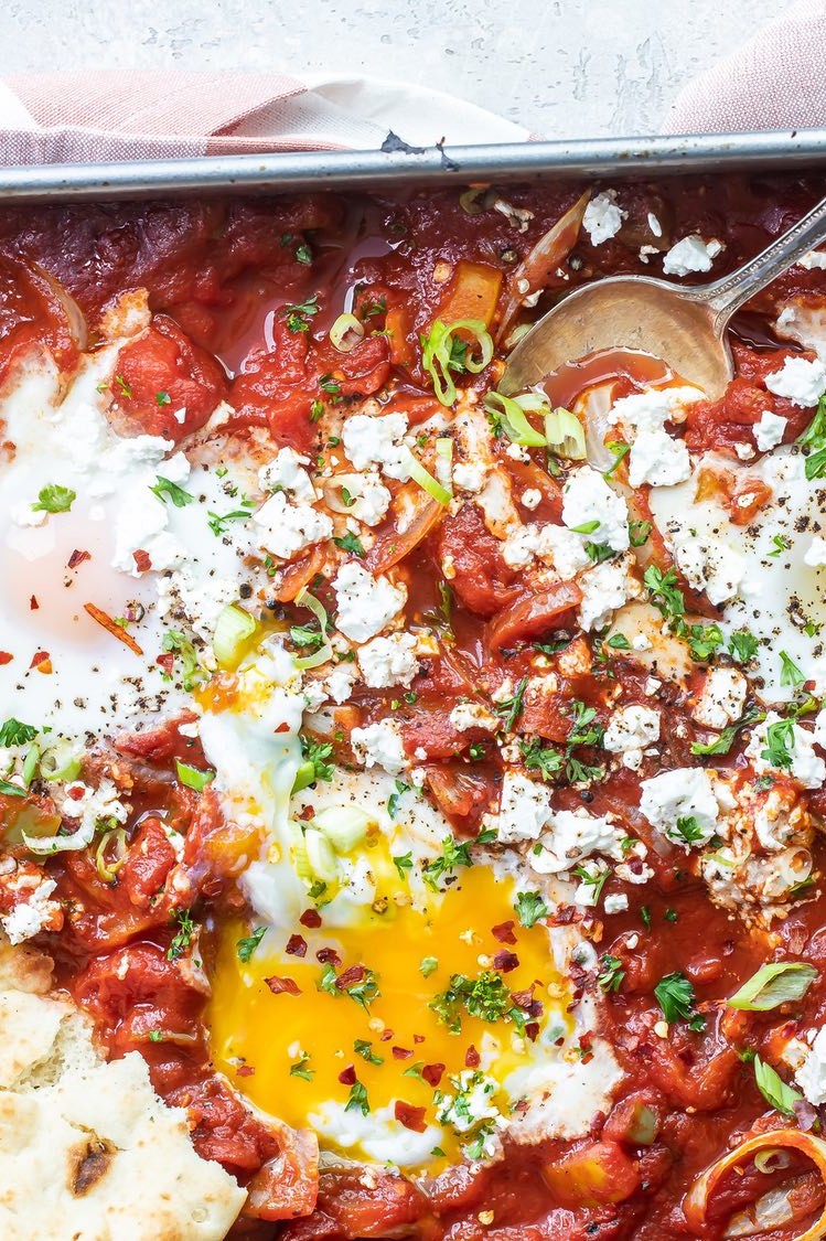 Shakshuka prepared in a sheet pan, topped with parsley and crumbled feta, and served alongside warm pita.