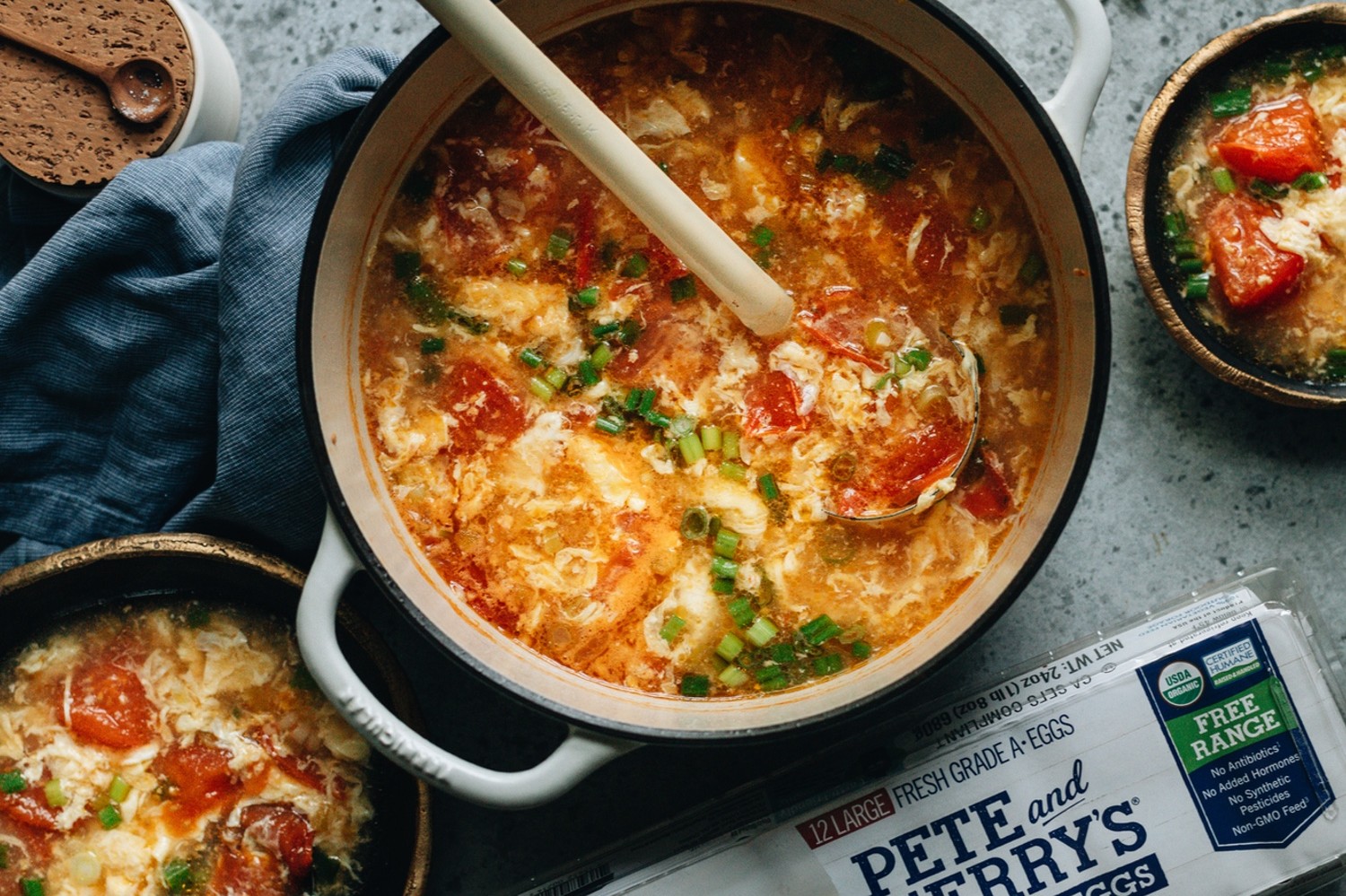 A pot of Chinese egg drop soup with freshly crushed tomatoes, chicken broth, and whisps of cooked egg garnished with sliced green onion. | peteandgerrys.com