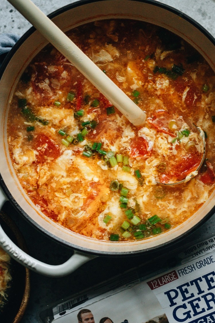 A pot of Chinese egg drop soup with freshly crushed tomatoes, chicken broth, and whisps of cooked egg garnished with sliced green onion. | peteandgerrys.com